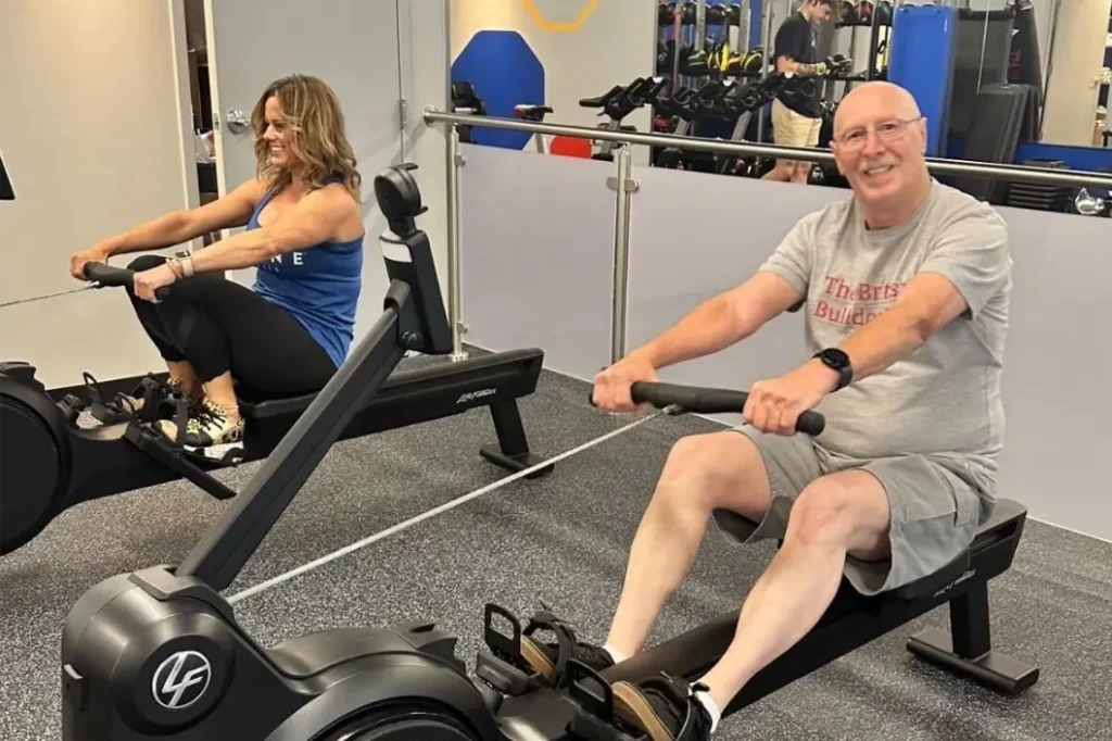 Woman and older man on a set rowing machines, working out.