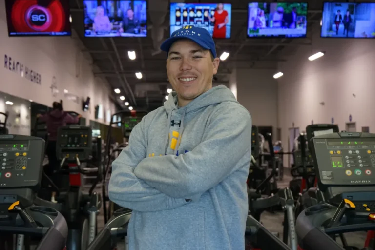 A smiling man, crossing his arms with a blue hitone hat.