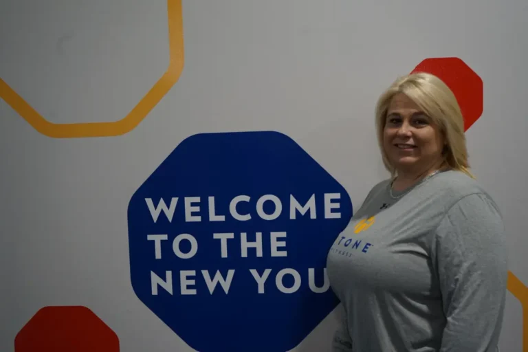 a woman smiling next to a gray wall.