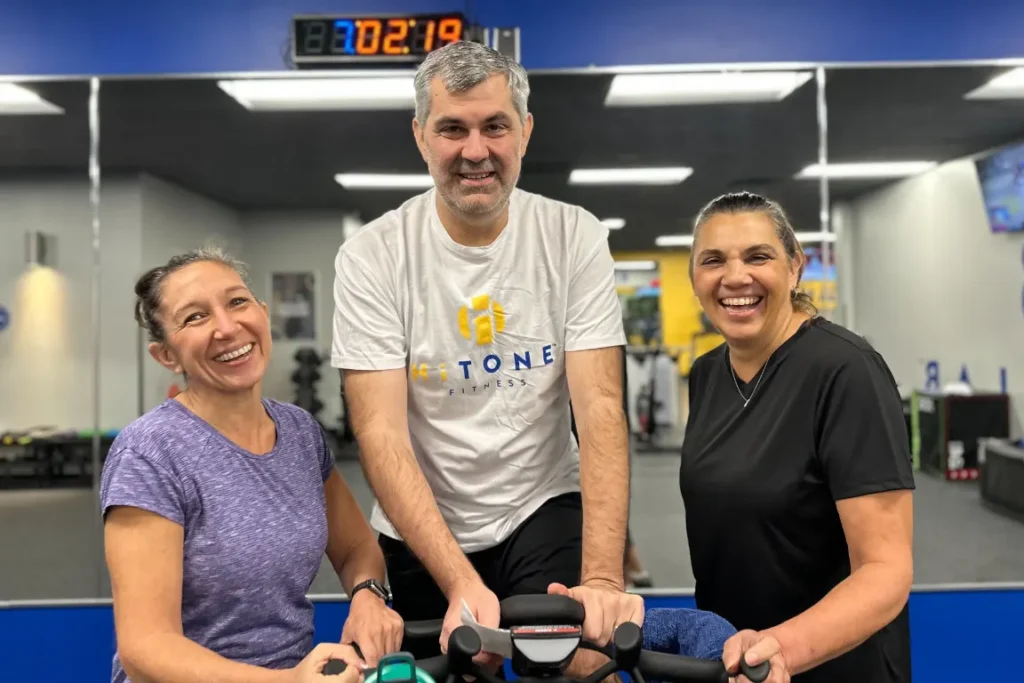 3 older people in a gym smiling at the camera.