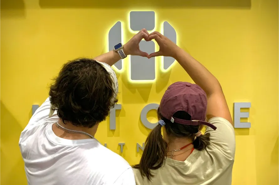two people forming a heart with their hand in front of the Hitone logo.