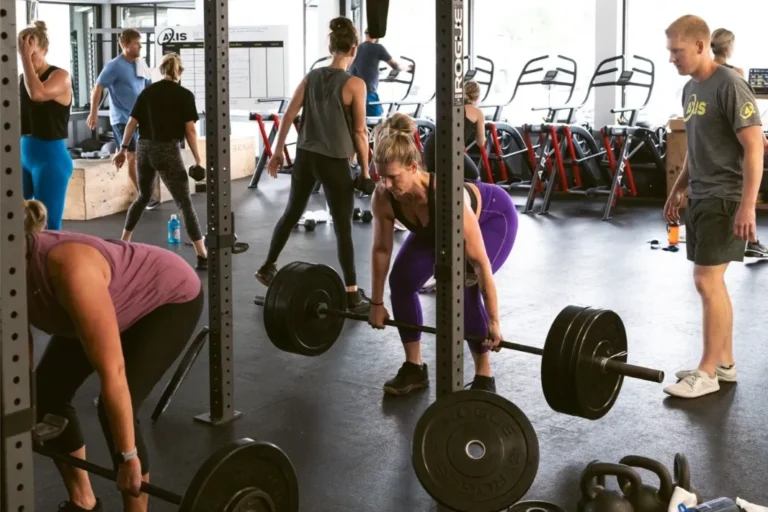 Multiple women working out and lifting weights, there is a personal trainer next to them.