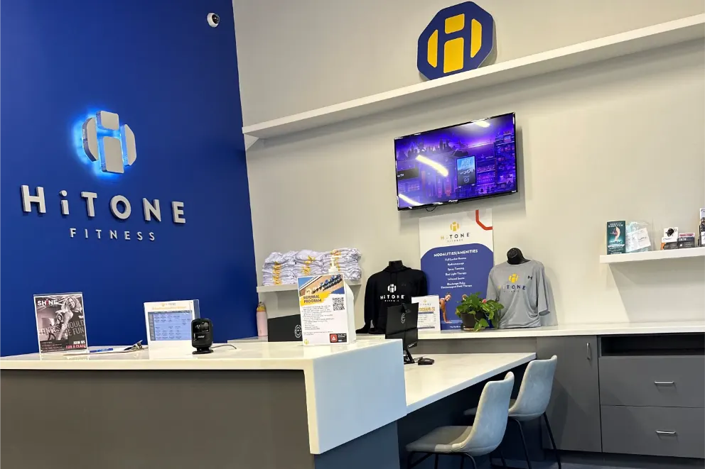A hitone fitness front desk, with a monitors and chairs.