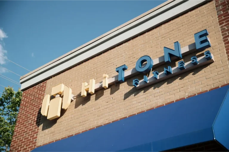 The yellow and blue storefront light letters of a HiTONE fitness gym.