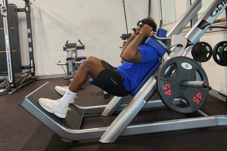 Blue shirted man doing squats on a machine.