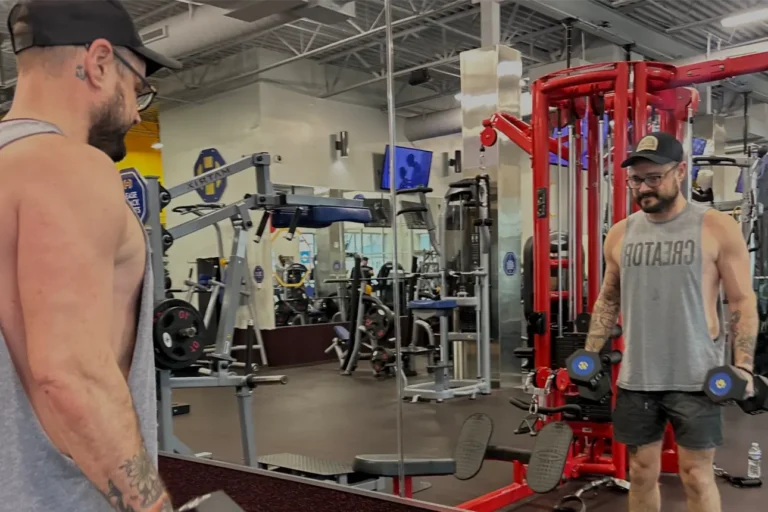 Man with hat and glasses working out in front of a mirror.