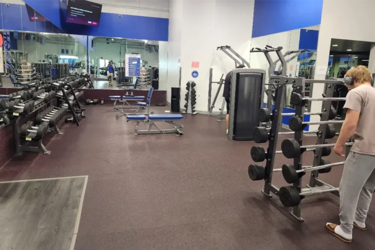 A man with headphones in front of a weight rack. More weight racks and benches in the background.