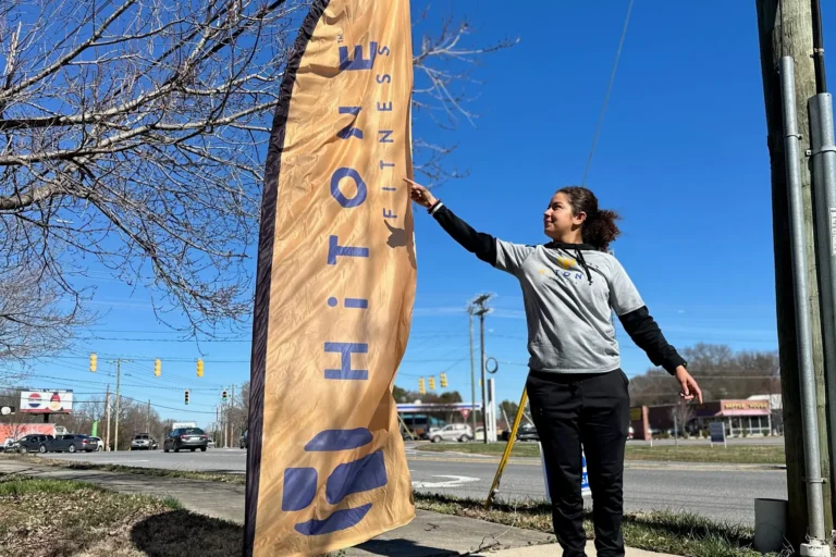 A smiling woman pointing at the HiTONE fitness sail flag.