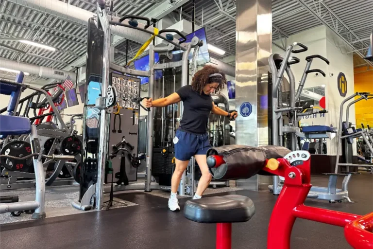 A woman with curly hair doing the cable chest fly exercise at a gym.