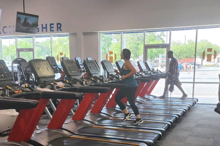 Nine treadmills and a woman in black leggings exercising on one of them.