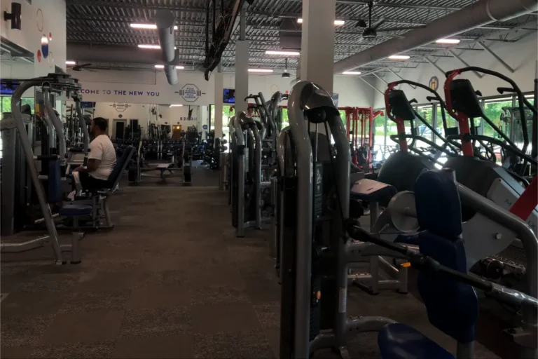 Multiple exercise equipment at a gym. A man in a white t-shirt is in the background.