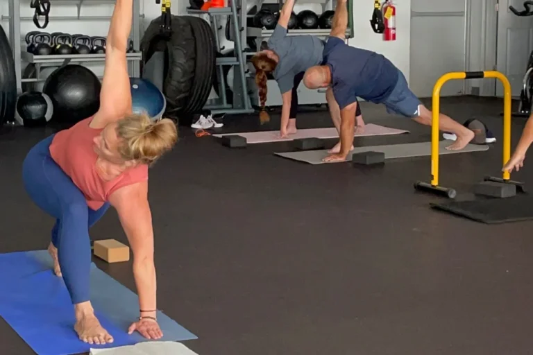 Three people doing revolved triangle yoga pose at a gym.