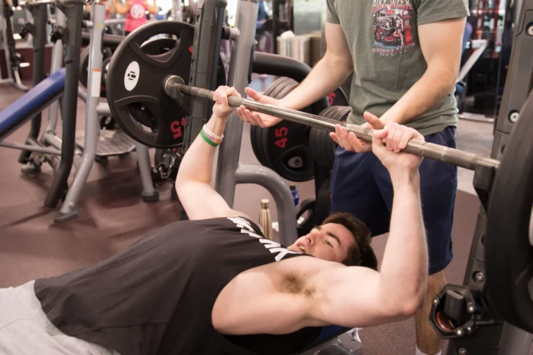 A man lying on a flat bench finishing a bench press series.