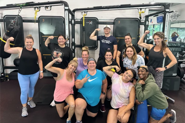 Eleven women and one man smiling and flexing their biceps for a picture.