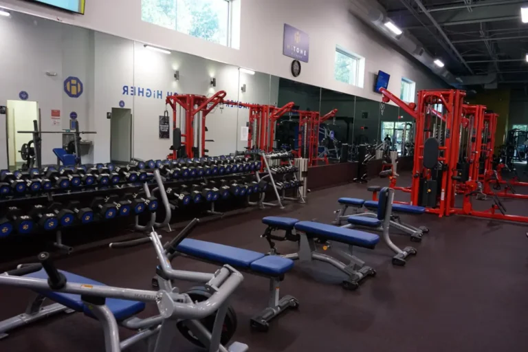 Four flat benches, weight racks, and a red functional trainer machine at a gym.