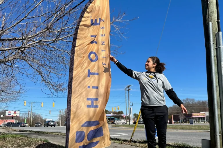 A smiling woman points at the HiTONE fitness sail flag.