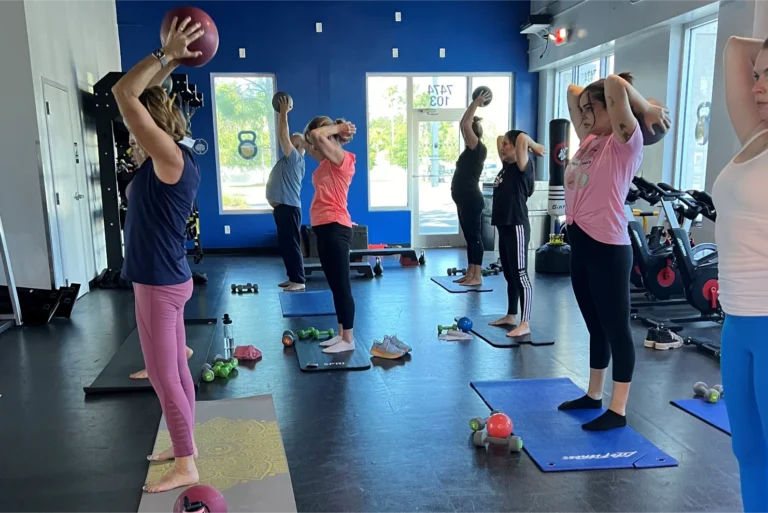 Six women of different ages and a man doing the overhead triceps extension exercise.