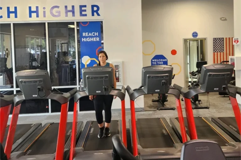 Four treadmills at a fitness center. A woman is standing on the machine in the center.