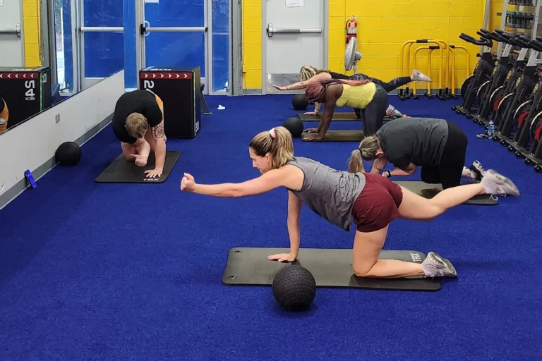 Five people doing the bird dog yoga pose in a room with a mirror.