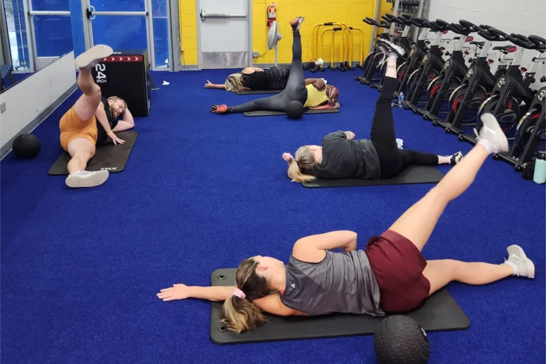 Four women and one man doing side-lying leg lifts at a gym.