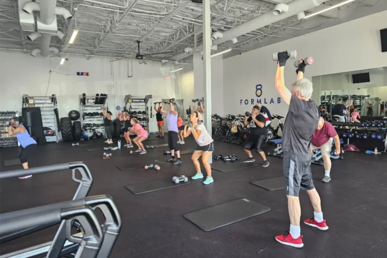 Male and female gym goers doing the dumbbell overhead press exercise at a fitness center.