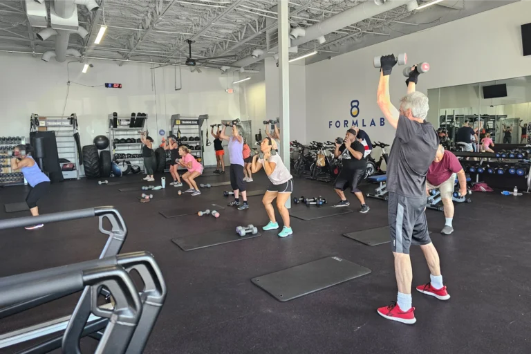 A group of senior gym goers doing the dumbbell overhead press exercise at a fitness center.