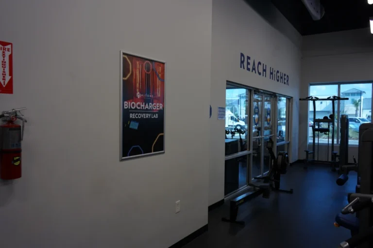 Inside of a gym with the Biocharger recovery lab framed image on the wall, rowing machine, and a pull-up station in the background.