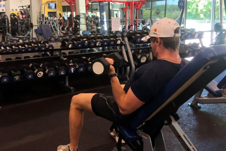 A man doing the seated incline dumbbell bicep curl exercise at a gym.