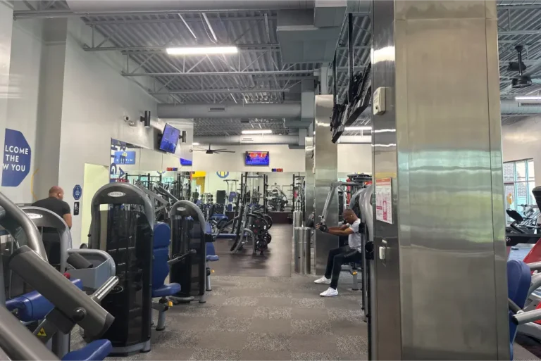 Various gym machines at a fitness center. One man is doing a seated exercise.