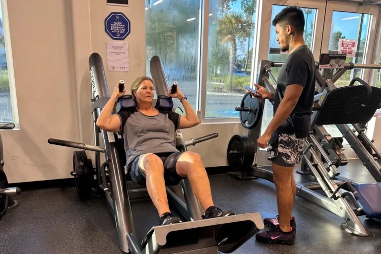 A male fitness instructor following a female gym goer progress on the leg press machine.