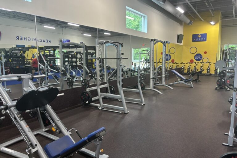 Angled leg press machine in the foreground and smith machines, benches, and exercise bikes in the background.