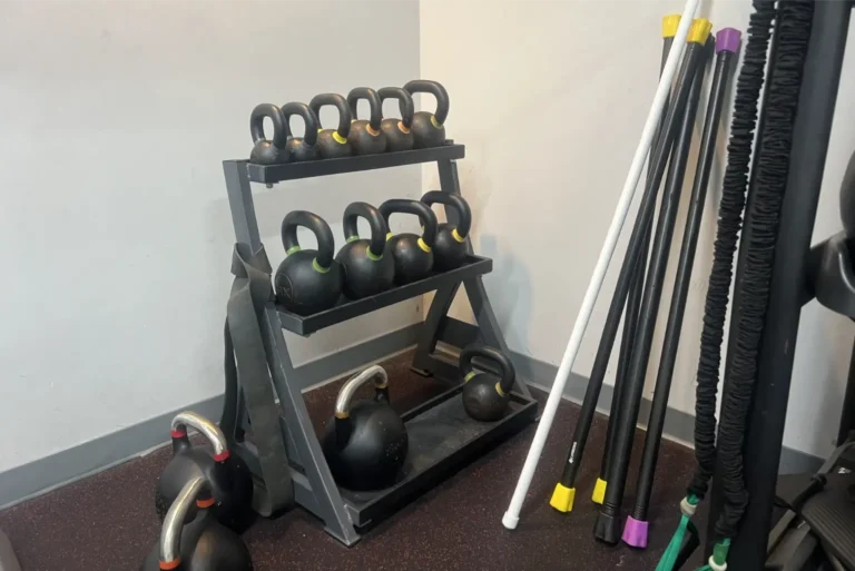 Kettlebells on a rack next to weighted bars and resistance bands.