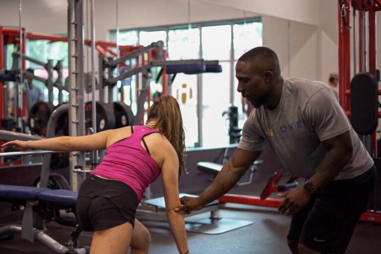 Male fitness instructor helping a female gym goer exercise at a fitness center.