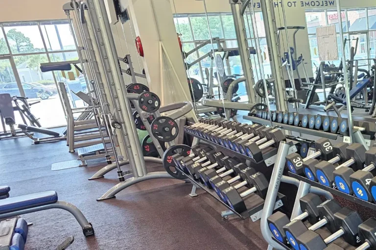 Weight rack with hex dumbbells in front of a dual adjustable pulley machine.