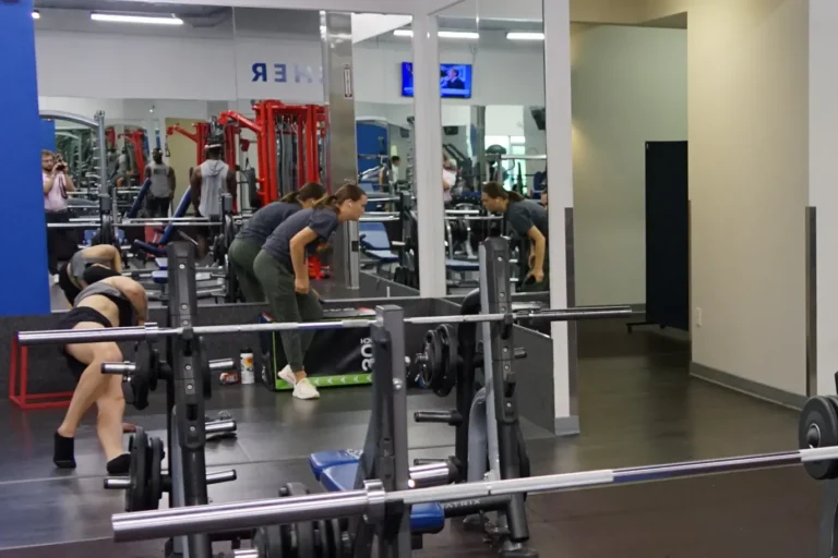 Two women exercise in front of the mirror at a gym.