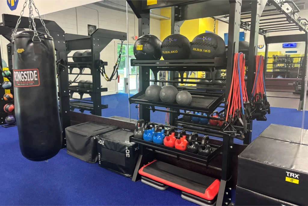 A boxing bag hanging next to a weight rack with medicine balls and kettlebells.