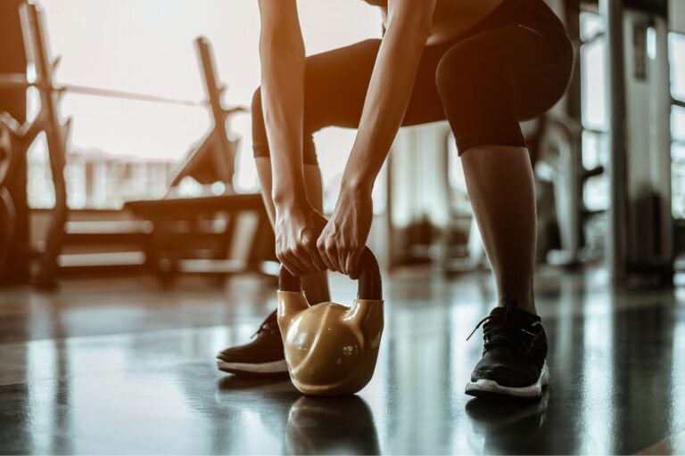 A woman squatting and holding a kettlebell that's on the floor.