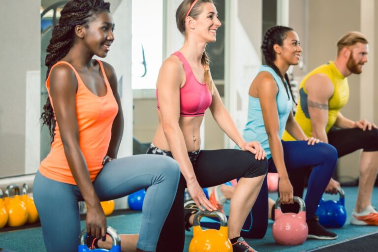 Three women and one man are smiling and preparing for the kneeling kettlebell hold exercise.