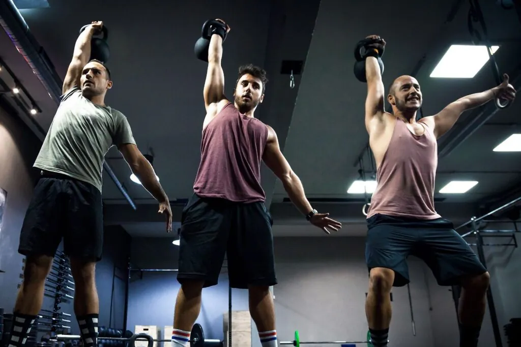 Three men doing the kettlebell overhead press exercise at a gym.