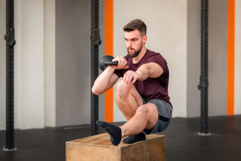 A man performing kettlebell pistol squat on a plyo box.