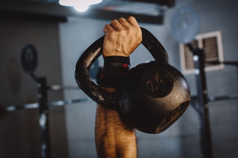 A man's arm and hand holding up a kettlebell with 24 engraving on it.