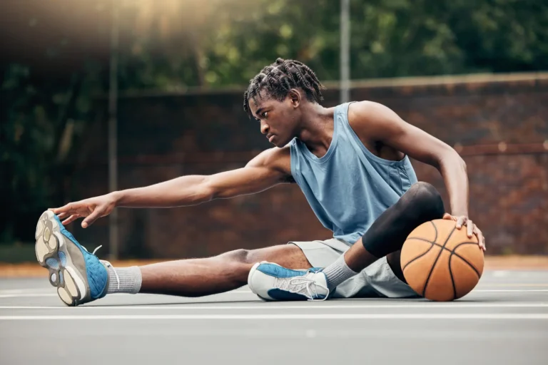 A man doing the seated hamstring stretch outside and resting his left arm on a basketball.