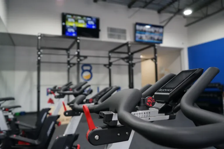 Handles of a stationary bike up close. There's a functional training rig in the background.