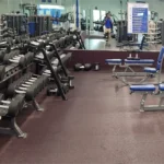 Dumbbells on weight racks and benches in front of a mirror at a gym.