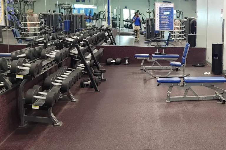 Dumbbells on weight racks and benches in front of a mirror at a gym.