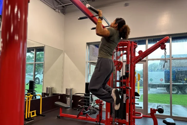 A woman doing pull-ups on a functional cable station inside a fitness center.