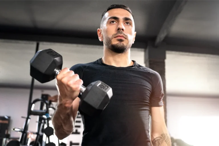 A man in a black t-shirt doing the standing bicep curl exercise with the hex dumbbell.