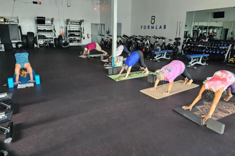 Six senior citizens on yoga mats doing the downward-facing dog pose at a gym.