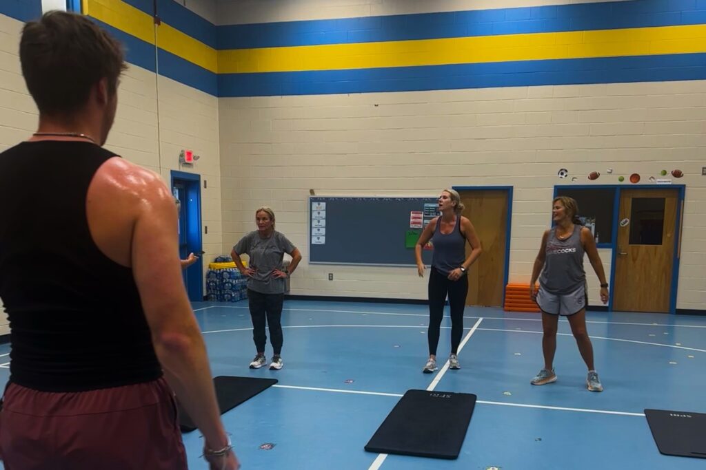 Man in the foreground is facing three women in the background who stand in front of their yoga mats.