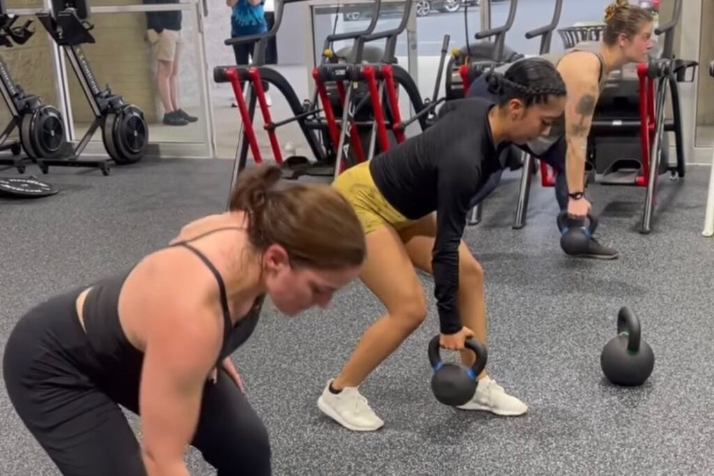 Three women doing the kettlebell deadlift exercise at a gym.